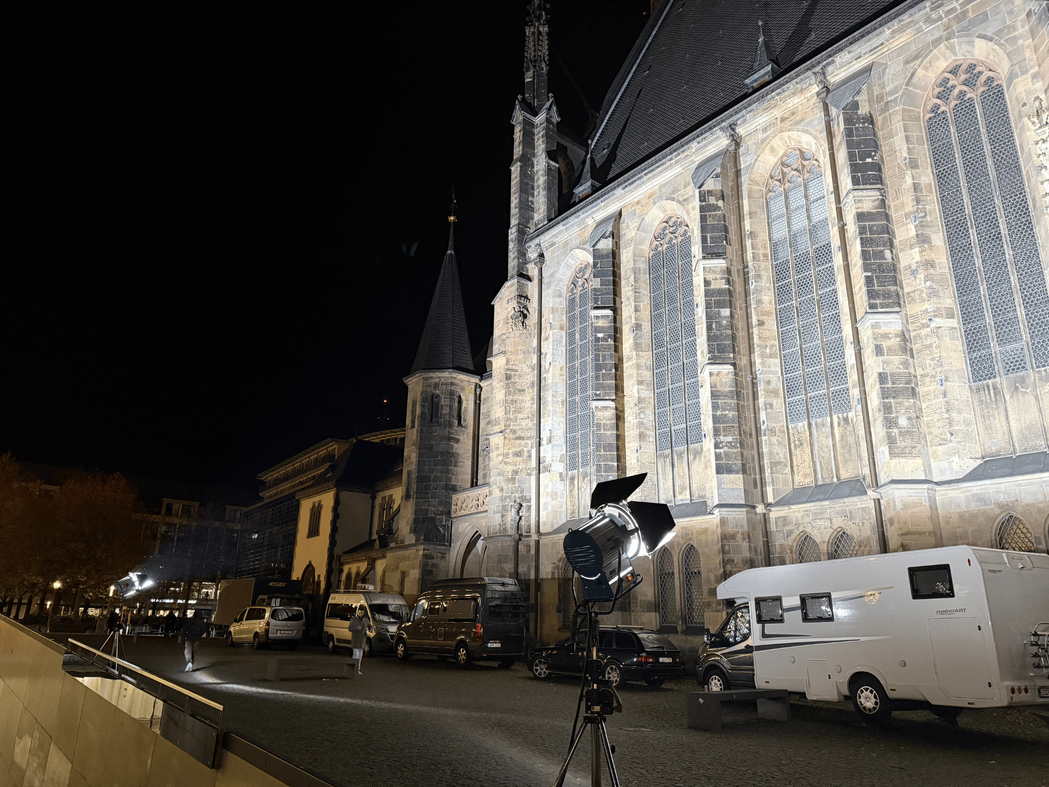 4 Livestream-Produktion mit Scheinwerfer und Fahrzeugen vor gotischer Kirche bei Nacht