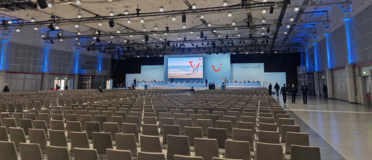 Großer Konferenzsaal mit leerem Publikumsbereich und professionell beleuchteter Bühne für die TUI Hauptversammlung 2025 mit Livestream-Setup