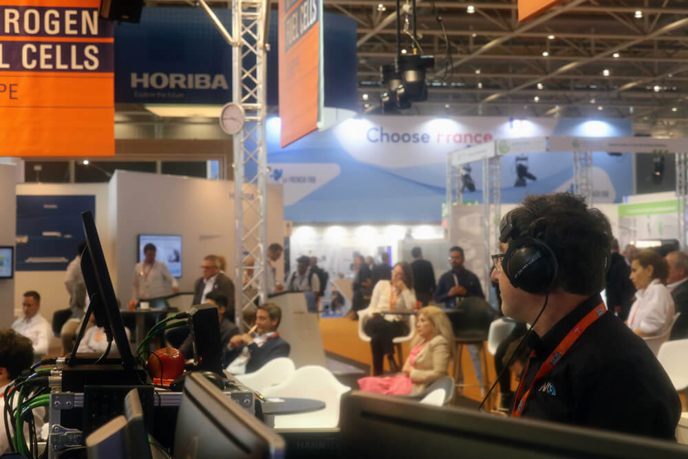 IMG_0679_194033864300079_2 NC3-Techniker mit Headset bei Live-Produktion und Livestreaming auf der Hannover Messe 2022, im Hintergrund Messestände und Publikum