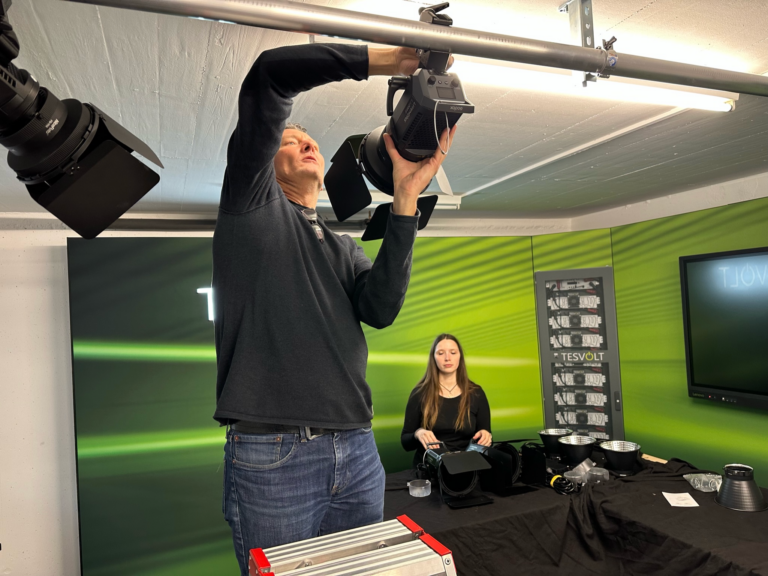Techniker montiert professionelle Kamera an Deckenhalterung in Studio mit grünem Hintergrund und Equipment für Event-Streaming