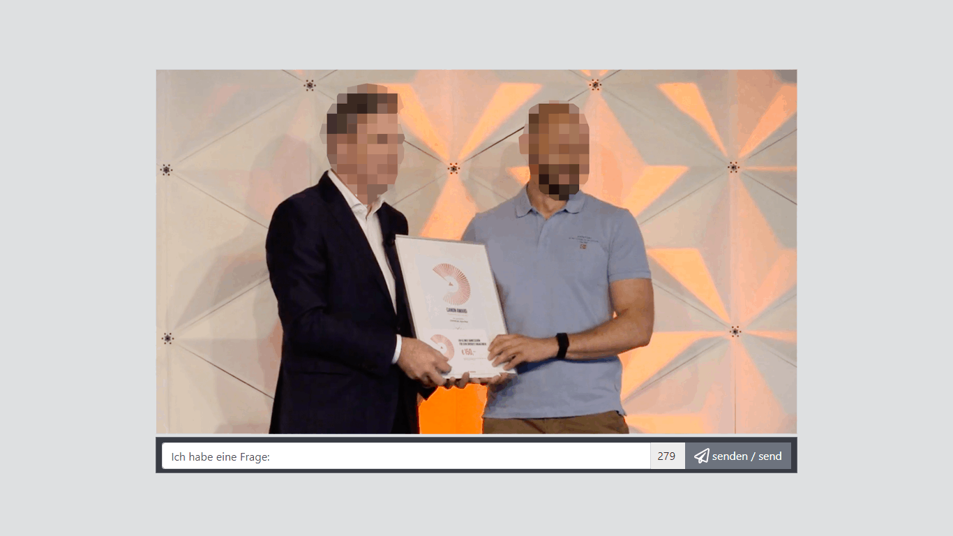 Zwei Männer präsentieren Green Award Certificate bei interner Veranstaltung mit Livestream-Chat-Interface
