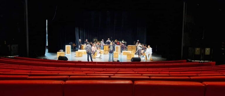 Bühnenfoto Musicalproduktion Bremen: rote Zuschauersitze und Akteure mit Bühnenaufbau, aufgenommen aus dem Saal