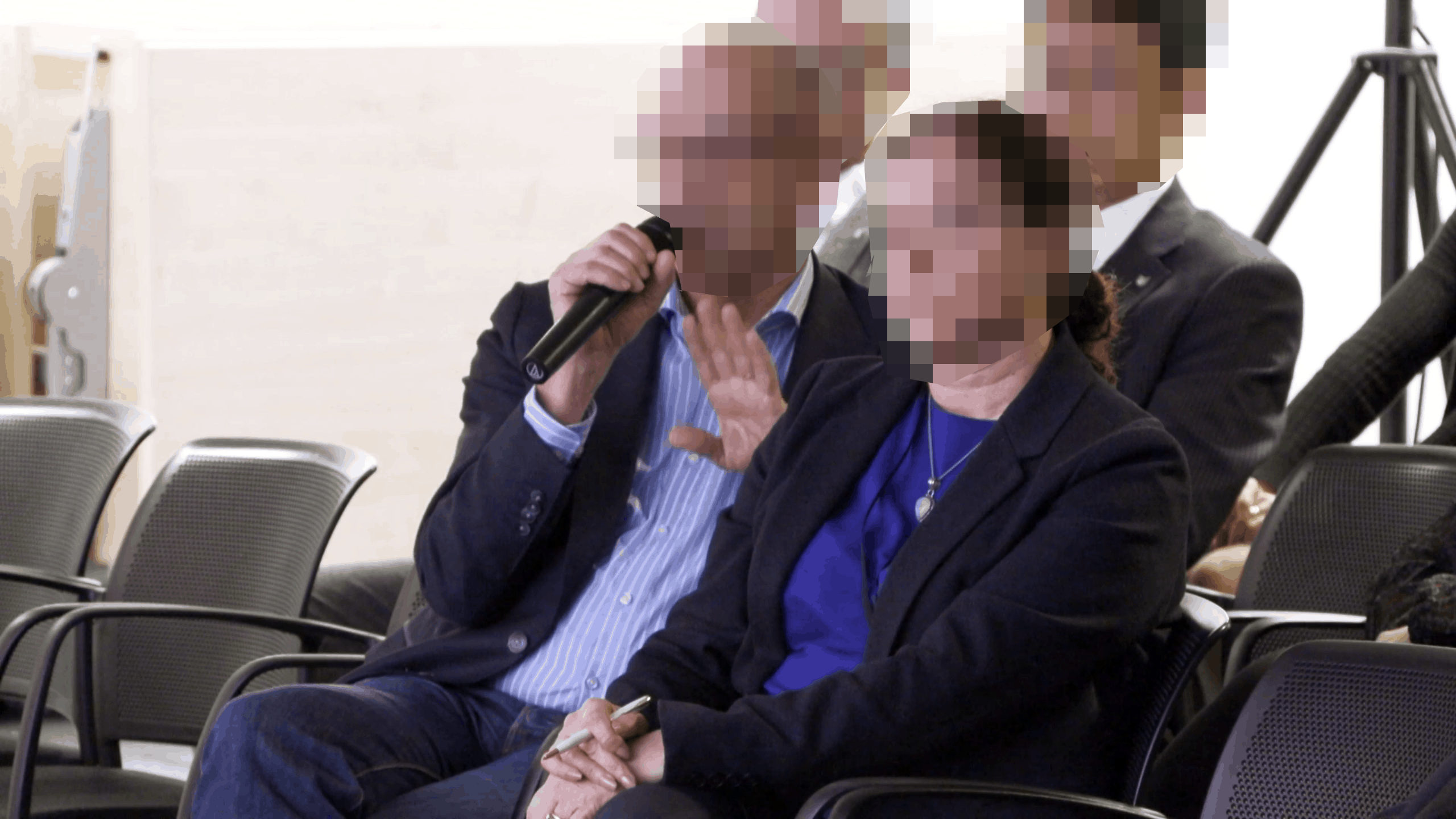 Verpixeltes Publikum bei Konferenz, Mann mit Mikrofon gestikuliert