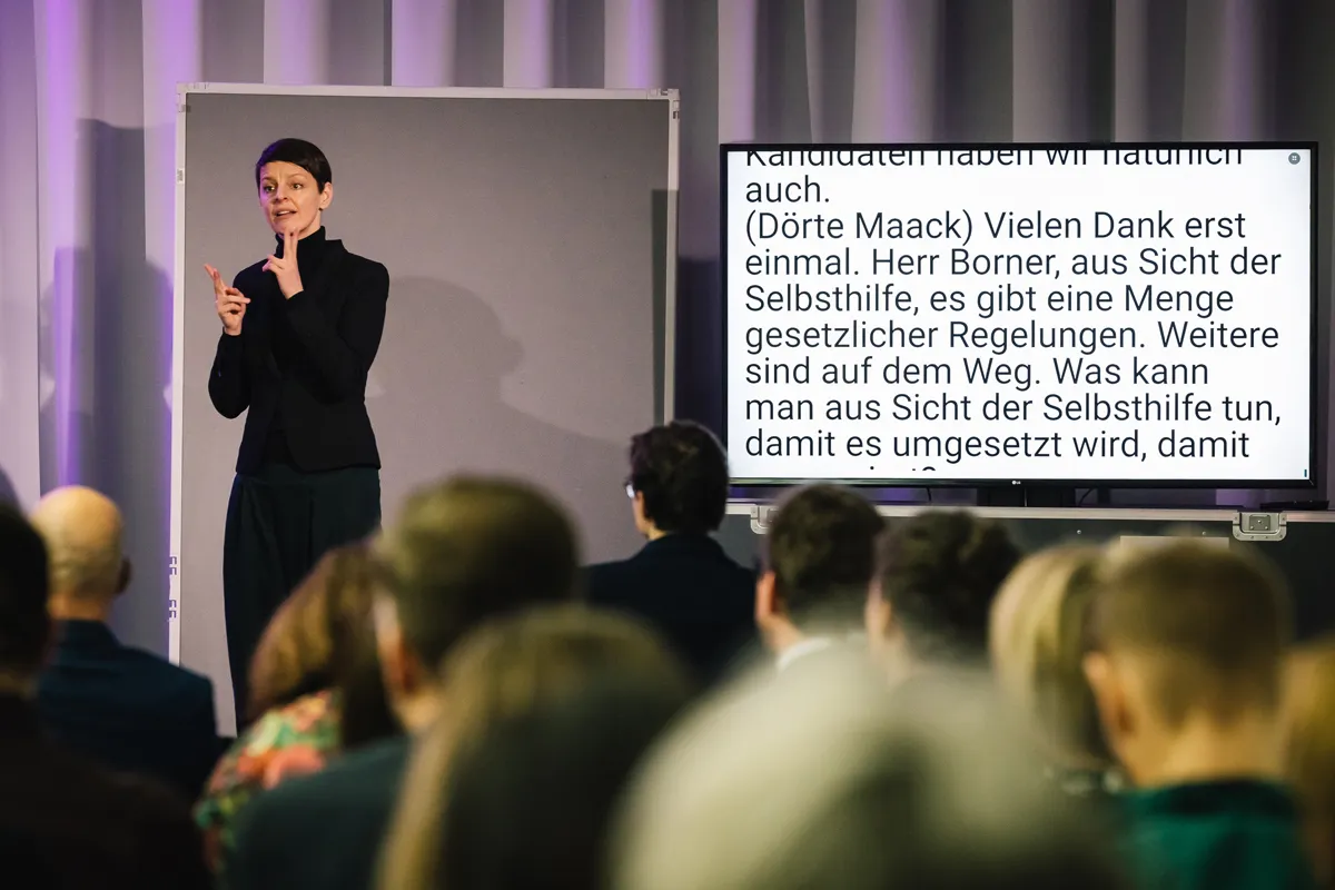 Jürgen Dusel und Gebärdensprachdolmetscherin bei barrierefreiem hybriden Event mit Live-Streaming