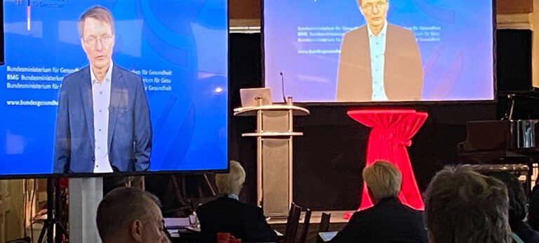 Karl Lauterbach auf Großbildschirmen bei hybriden Event der Sepsis Stiftung mit Publikum und Bühne