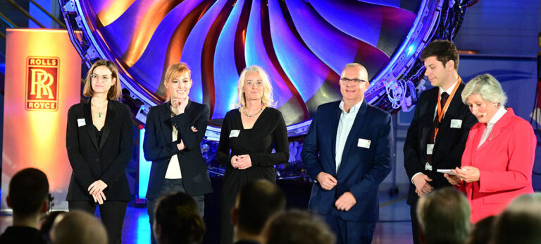 Preisträger auf Bühne bei hybrider Medienpreis-Verleihung vor Rolls-Royce Jet-Triebwerk Kulisse