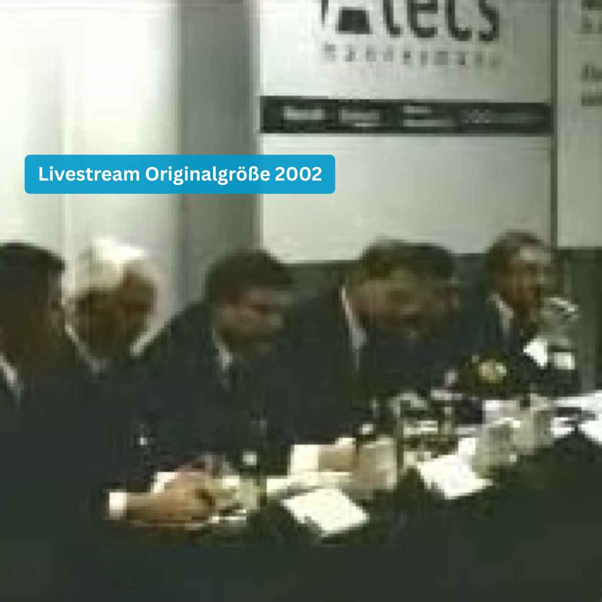 Historische Konferenzszene 2002 mit NC3 Livestream-Overlay und Teilnehmern am Tisch
