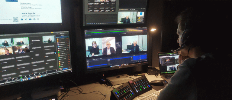 Techniker in der Remote-Regie steuert Hybrid-Event mit mehreren Monitoren, Video-Feeds und ATEM-Mini-Controllern