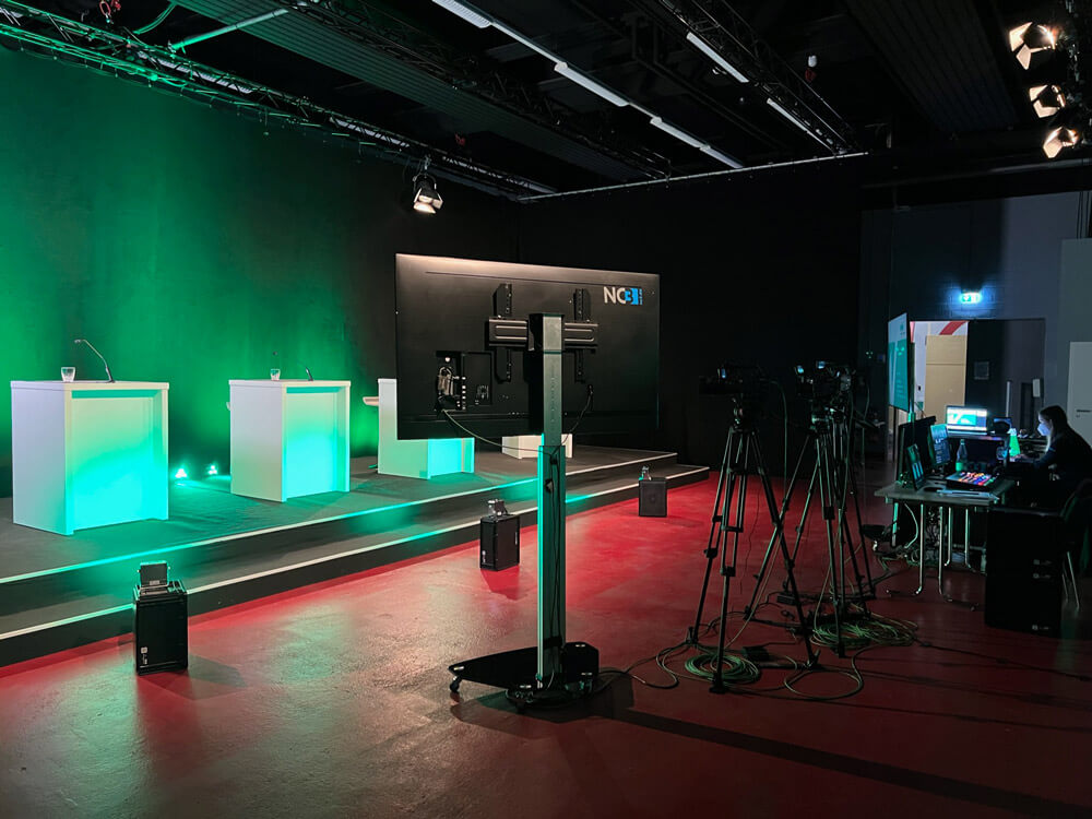 verbio-hv-studio1-ansicht-veranstaltung-live-streamen NC3 Studio mit Bühne, beleuchteten Pulten, Green Screen und mehreren Kameras für professionelle Livestreams und Veranstaltungen