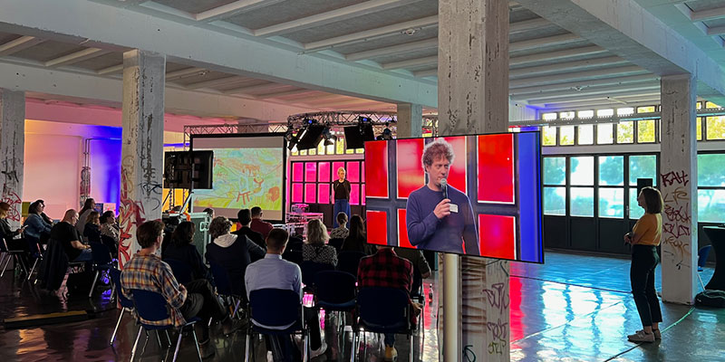 Konferenzraum mit Publikum, Bühne und großer LED-Videowand bei KidsCon 2022, Speaker auf Display